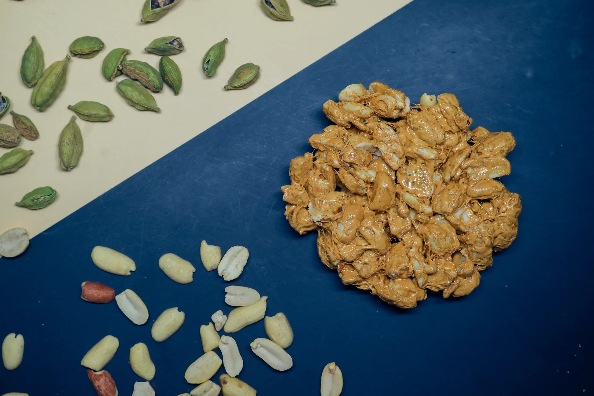Cardamom tilpatti made with peanuts and jaggery, surrounded by whole green cardamom pods and peeled peanuts on a dual-tone background, surrounded by whole green cardamom pods and peeled peanuts on a dual-tone background