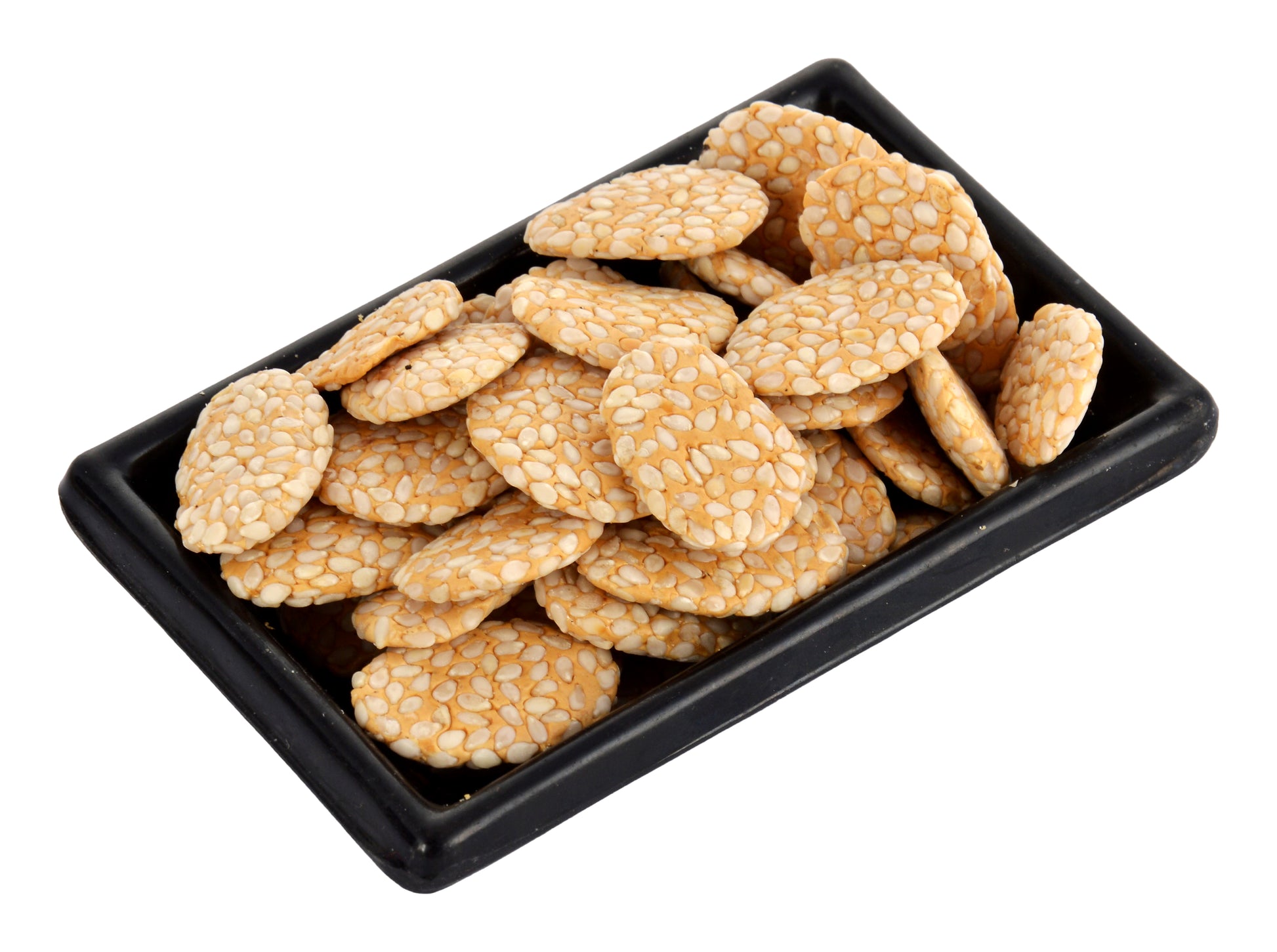 A black tray containing traditional Indian jaggery rewri, which are crunchy snack-like cakes with a nutty flavor and a textured appearance.