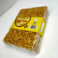 Packaged Rice Chikki snack with a yellow label on top, visible through the transparent packaging.